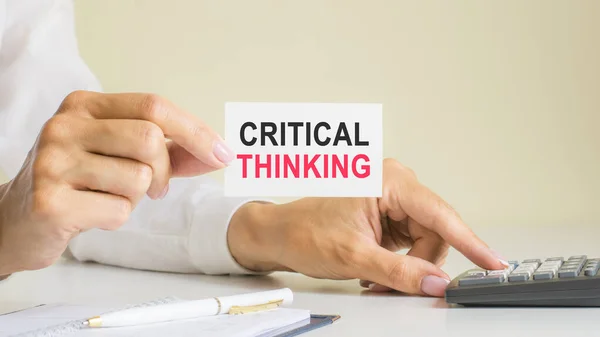 critical thinking inscription on white card paper sheet in hands of woman. red and black letters on white paper. business concept, grey backgrond