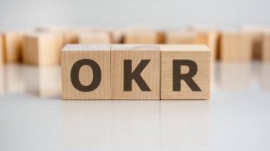 Tahta blokta OKR kelimesi yazıyor. OKR sözcüğü, gri masanın üzerinde duran ahşap yapı taşlarından oluşur, iş kavramı. OKR Hedefler ve Anahtar Sonuçları kısaltması