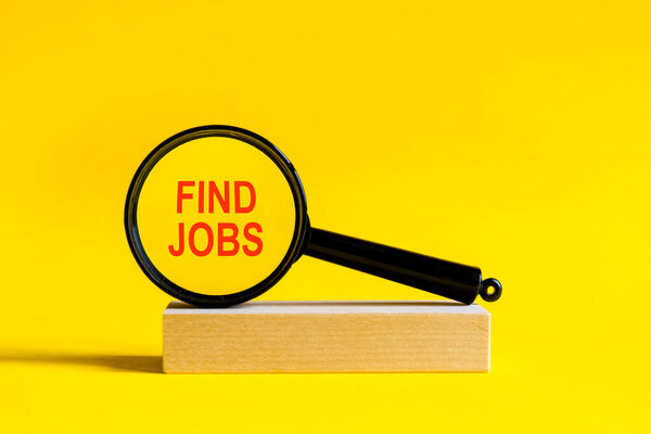 надпись найти работу через лупу на желтом фоне. Увеличительное стекло монтируется на деревянном подставке на столе