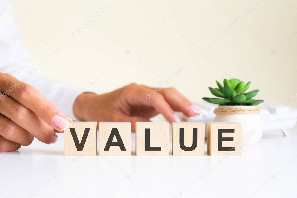 Businessman hand holding wooden cube block with Value business word on table background. Mission, Vision and core values concept.