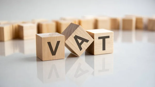 VAT - Value Added Tax acronym concept on cubes, gray background. Reflection on the mirrored surface of the table. Selective focus.