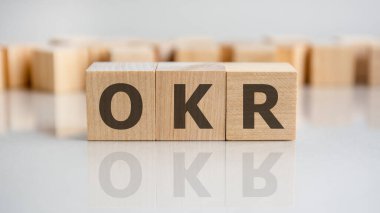 Tahta blokta OKR kelimesi yazıyor. OKR sözcüğü, gri masanın üzerinde duran ahşap yapı taşlarından oluşur, iş kavramı. OKR Hedefler ve Anahtar Sonuçları kısaltması