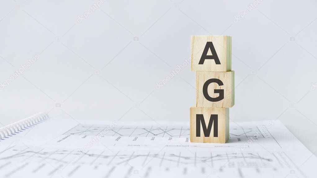 three stone cubes on the background of white financial statements, tables with the word AGM Annual general meeting. Strong business concept. Gray background.