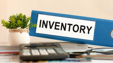 INVENTORY - mavi klasör hesap makinesi, kalem ve yeşil saksı bitkisi ile ofis masasında. İş, finans, eğitim, denetim ve vergi kavramları için kullanılabilir. Seçici odak.