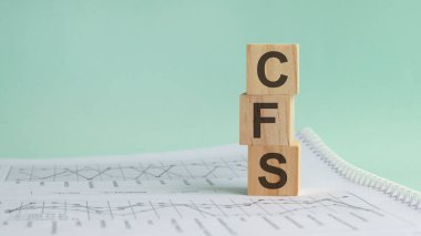 Beyaz mali tabloların arka planında üç taş küp, CFS harfli masalar - Acronim Consolidated Financial Statement. Güçlü iş konsepti. Gri arkaplan.