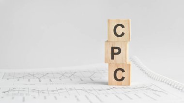 Beyaz finansal tabloların arka planında üç taş küp, üzerinde CPC yazan masalar - Acronim Post Per Click. Güçlü iş konsepti. Gri arkaplan.