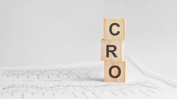 three stone cubes on the background of white financial statements, tables with the word CRO - acronim Conversion Rate Optimization. Strong business concept. Gray background.
