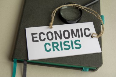 Gri defterde bir büyüteç ve üzerinde ekonomik kriz yazan seçici odaklı beyaz bir kağıt var.