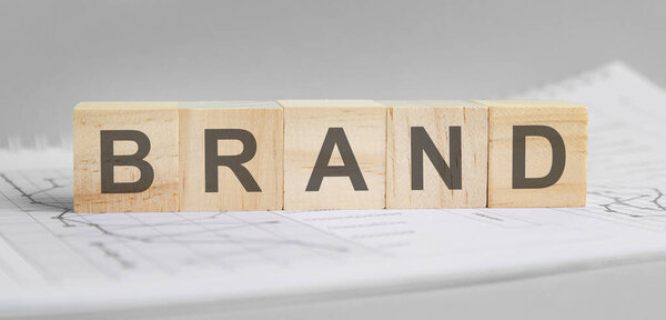 Бренд написан на светлых деревянных блоках. слово расположено на листе с графиками и диаграммами. бизнес концепция. серый фон