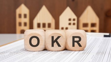 Three wooden cubes with OKR letters placed on spreadsheet, representing objectives and key results in business planning, productivity and performance measurement strategy