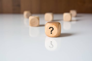 Parlak beyaz arka planda soru işareti olan tahta bir bloğa yakın plan. Belirsizlik, soruşturma ya da karar verme kavramı.