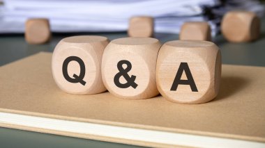 Q işaretli üç doğal tahta blok küp ve A kapalı bir defter üzerine kurulmuş ofis belgeleriyle. Resim diyalog, müşteri desteği, öğrenme ve bilgi paylaşımını iletir.