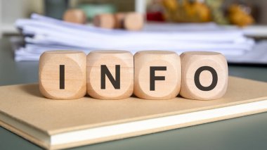 I-N-F-O olarak işaretlenmiş dört tahta blok kübü kapalı bir defterin üzerinde oturuyor ve arkasında yavaşça bulanık dökümanlar var. Resim bilgi, veri paylaşımı, bilgi yönetimi ve profesyonel iletişim temalarını anımsatıyor.
