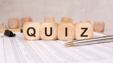 Quinz 'i ofis masasında kalem ve belgelerle heceleyen tahta küplerin kapatılması, tarafsız bir çalışma alanında bilgi testi, öğrenme, araştırma veya eğitim kavramını sembolize ediyor