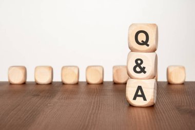 Q harfleriyle dikey olarak dizilmiş üç doğal tahta küp ve arka planda bulanık tahta bloklar olan ahşap bir yüzey üzerinde A. İş, eğitim ve teknoloji bağlamları için yardım, bilgi alışverişi, iletişim ve rehberlik kavramları