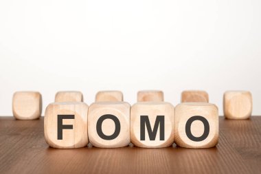 Ahşap bloklar masa üstünde fomo yazımını engelliyor, arka planda bulanık tahta küplerle en az stüdyo sahnesi, tüketici endişesi için görsel metafor, pazarlama aciliyeti, sosyal medya baskısı, karar verme mekanizması