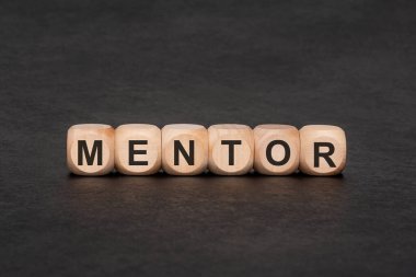 İş ve kişisel gelişim konsepti akıl hocalığı. Tahta harf blokları siyah bir levha gibi bir yüzey üzerinde düzenlenmiş kelime MENTOR oluşturur. Liderlik, kariyer koçluğu, destek ve bilgelik transferini sembolize eder..
