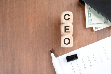 Tahta bir arka planda dikey tahta bloklar CEO 'su. Sahnede Amerikan dolarları ve takvimi olan siyah deri bir cüzdan yer alıyor. Yürütme yönetimi, mali yönetim ve kurumsal karar verme mekanizmasını temsil eder