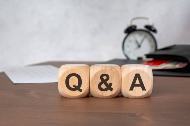 Tahta bir masaya odaklanarak soru-cevap kodlayan üç tahta küpün yakın çekimi. Bulanık arka planda siyah bir çalar saat, kırmızı kartlı bir cüzdan ve bir takvim sayfası yer alıyor. Sık sorulan sorular için kavramsal resim, profesyonel danışma