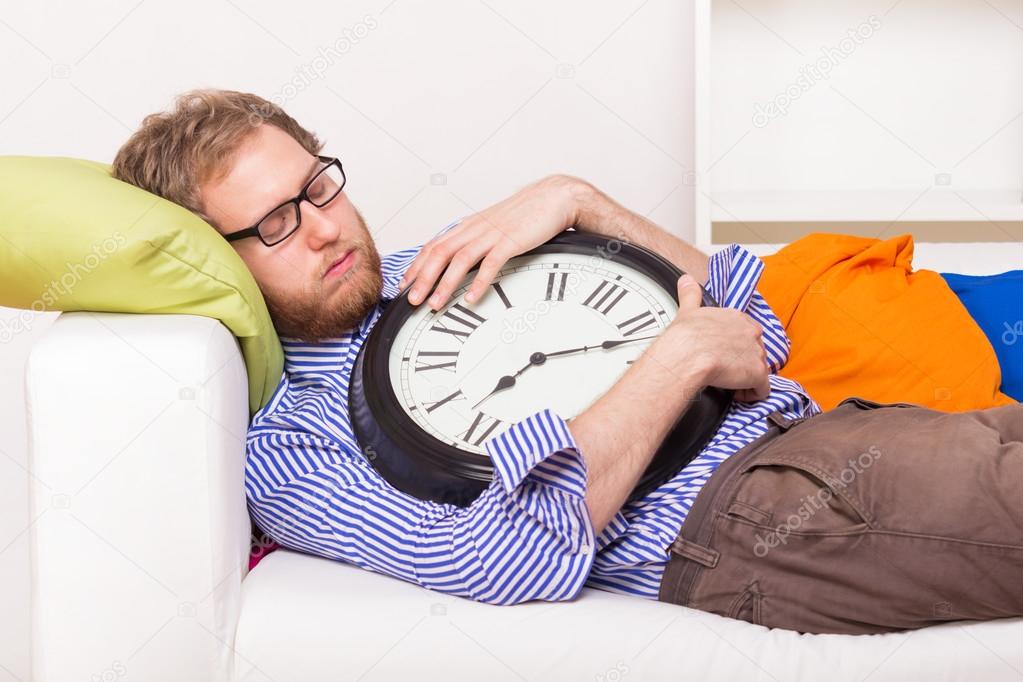 Young man sleeping on the couch with big clock 
