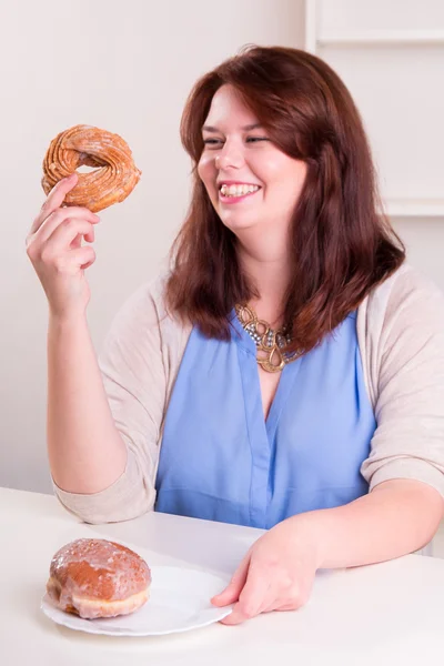 Knubbig kvinna med en donut i hennes hand vid bordet — Stockfoto