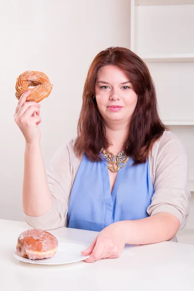 Donna grassoccia che tiene una ciambella in mano al tavolo — Foto Stock