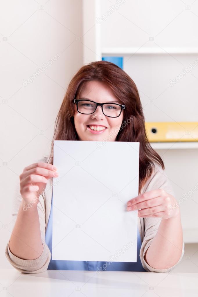Plump woman at a table holding a white sheet of paper with copy 