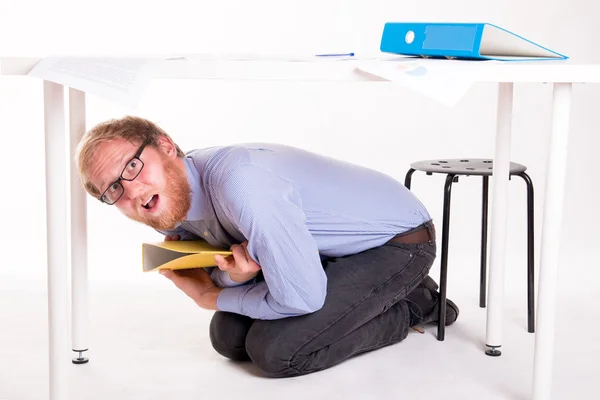 Verängstigter Mann kauert unter Schreibtisch im Büro — Stockfoto