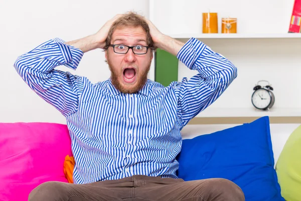 Shocked man screams in horror and sitting on the sofa — Stock Photo, Image