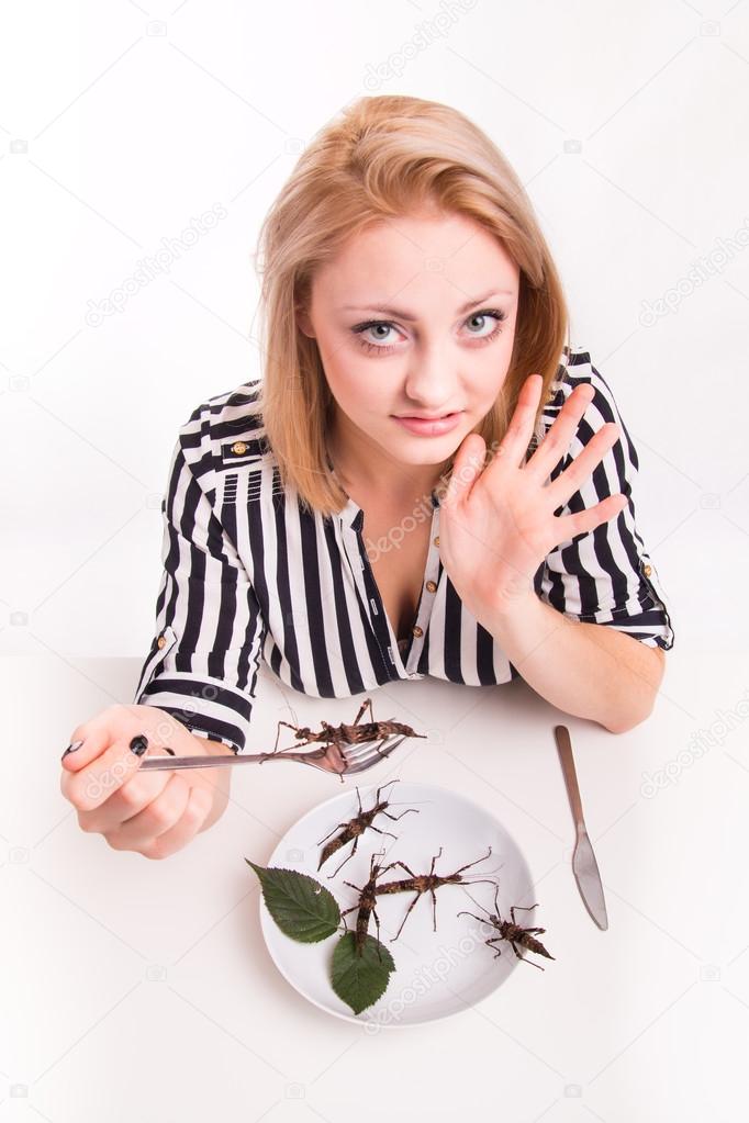 Disgusted woman eating insects with a fork in a restaurant