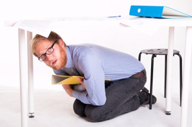 man huddled under a desk in the office clipart