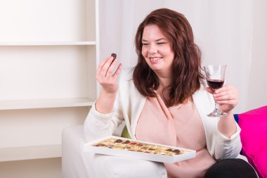 Plump woman eating chocolate with wine clipart