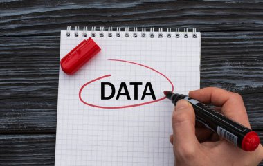 Bir kadının eli beyaz bir çarşafa siyah ahşap arka planda DATA kelimesini yazar. İş konsepti