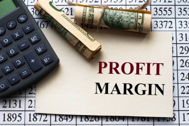 PROFIT MARGIN - words on white paper against the background of a table of numbers with a calculator and banknotes. Business and finance concept clipart