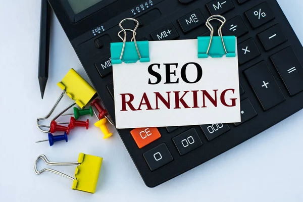 SEO RANking - hesap makinesi, düğmeler ve sarı kırtasiye klipleriyle beyaz arka planda klipsleri olan beyaz bir sayfa üzerinde kelimeler. İnternet kavramı