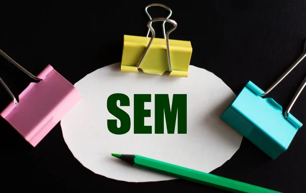 SEM (Search Engine Marketing) - word on white paper with multicolored clips and green pencil. Business concept