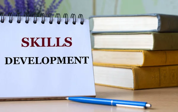 SKILLS DEVELOPMENT - a word in a notebook against the background of old books with a pen. Education concept.