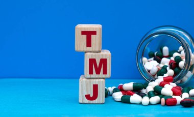 Küplerle ilgili TMJ kelimesi mavi arka planda ve bir kavanoz tabletle. Tıbbi konsept.