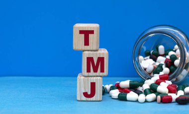 TMJ word on cubes on a blue background with a jar of tablets. Medical concept. clipart