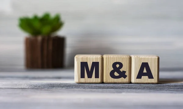 M&A (Mergers and Acquisitions) - word on wooden cubes against the background of a light board with beautiful divorces and a cactus. Business concept