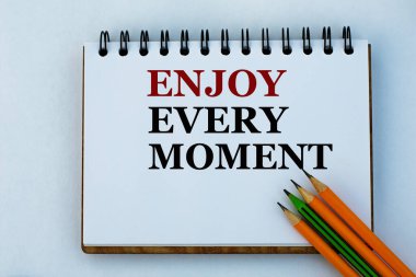 Her anın tadını çıkar. Beyaz bir not defteri ve kalemle yazılmış kelimeler. Başarı ve pozitif konsept