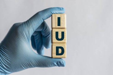IUD (Intrauterine device), mavi eldiven içindeki bir elle tutulan küplerin kısaltmasıdır. Tıbbi konsept.