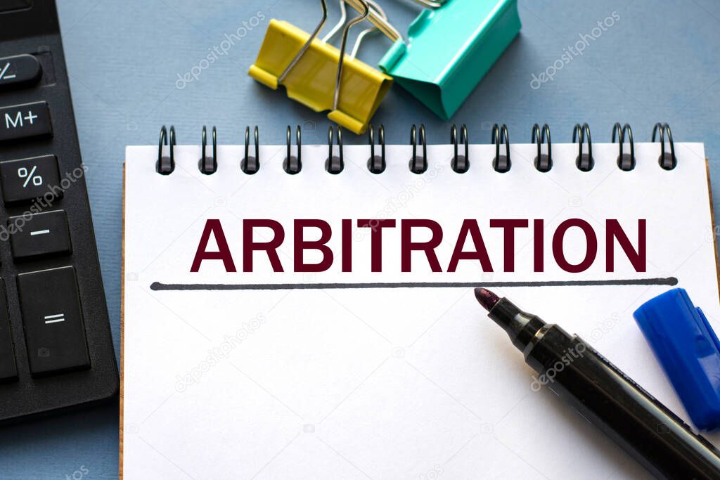 ARBITRATION word is written in a notebook with a marker, calculator, clamps and cactus. Business concept