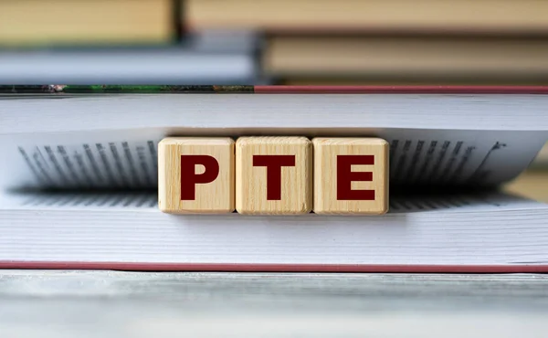 PTE (Pearson Test of English) - word on wooden cubes against the background of the open book. Info concept