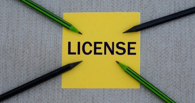 Lisans - gri arka plan ve kalemler üzerinde sarı bir kağıt parçası üzerinde kelime. İş konsepti