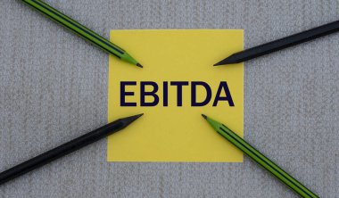 EBITDA (Faizden Önce Gelirler, Vergiler, Değerlendirme ve Amortisman) - gri arka plan ve kalemlerdeki sarı bir kağıt parçasında kısaltma. İş konsepti