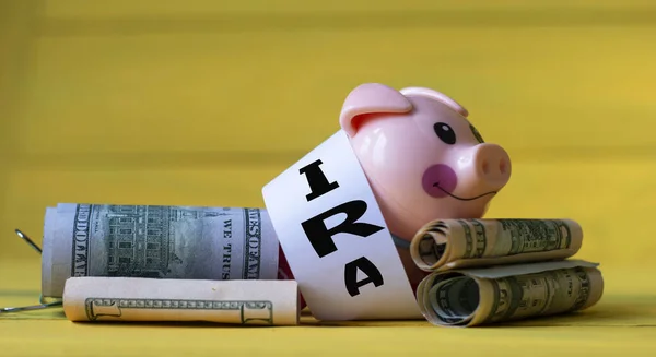 IRA (Individual Retirement Account) - acronym on a white strip of paper on a piggy bank pig on a yellow background with banknotes