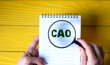 Sarı ahşap arka planda CAO sözcüğünün üzerinde bir kadının eli büyüteç tutuyor. İş konsepti