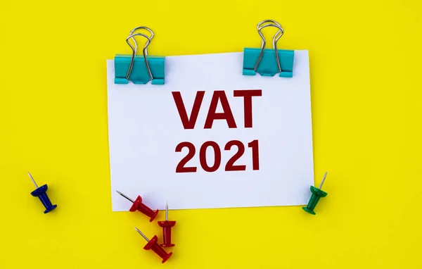 VAT (Value added tax) 2021 - acronym on white paper with clips on yellow background with buttons and pencil. Technology and business concept