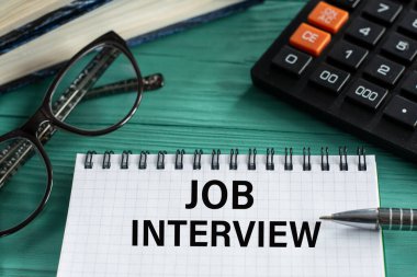 JoB Röportajı. Hesap makinesi, kalem ve gözlüklü, ahşap yeşil arka plandaki not defterindeki kelimeler. İş konsepti